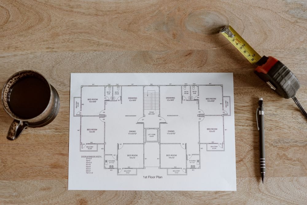 Printed floor plan on a wooden desk with a pen and measuring tape